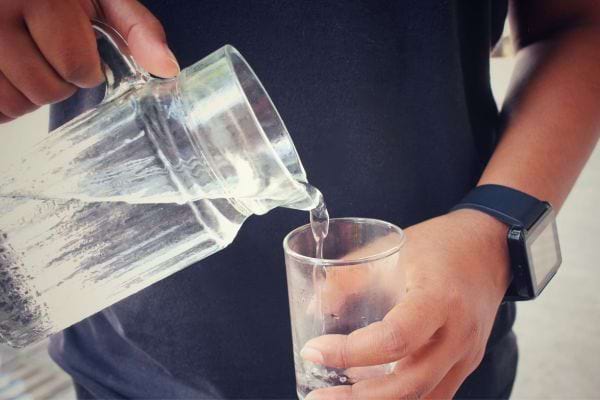 Main verse de l'eau d'une carafe dans un verre tenu par un homme.