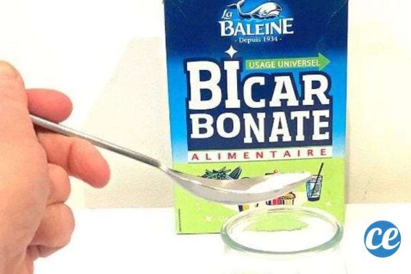 une personne tient une cuillère de bicarbonate de soude devant un paquet La Baleine
