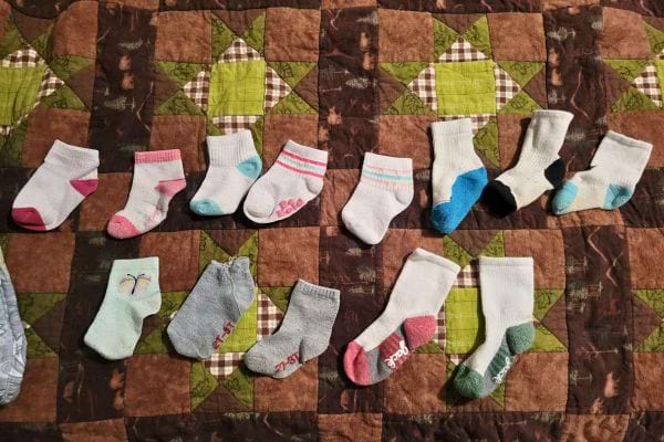 Petites chaussettes de bébé alignées sur une couverture marron.