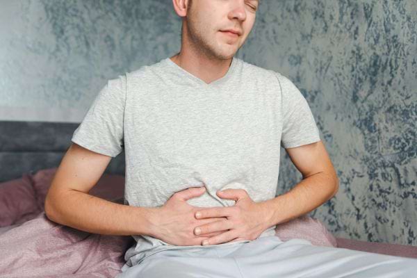 Un homme en t-shirt gris avec les mains sur le ventre.