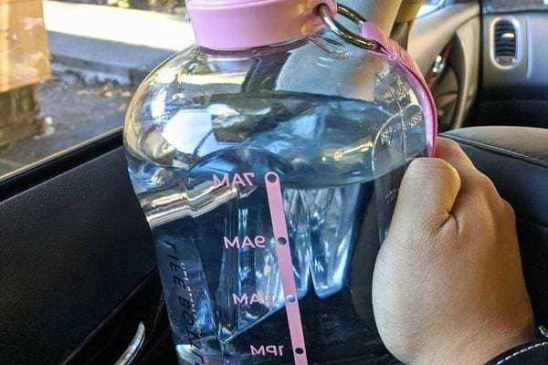 Main tenant une grande gourde rose remplie d'eau dans une voiture.