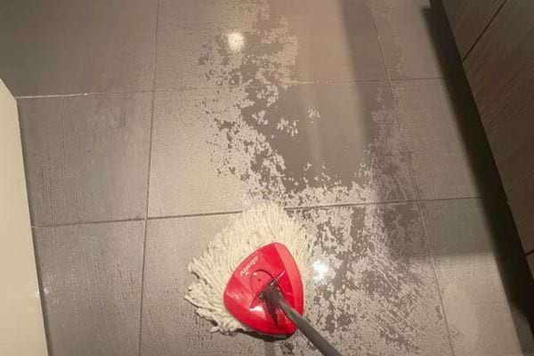 Un mop rouge sur un carrelage gris avec des traces d'eau.