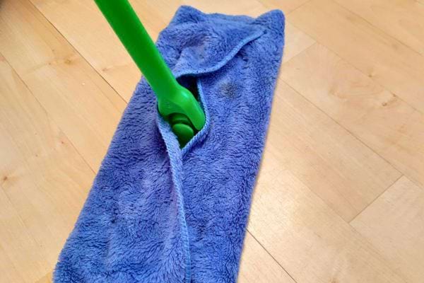 Une serpillière bleue avec un manche vert sur un sol en parquet clair.