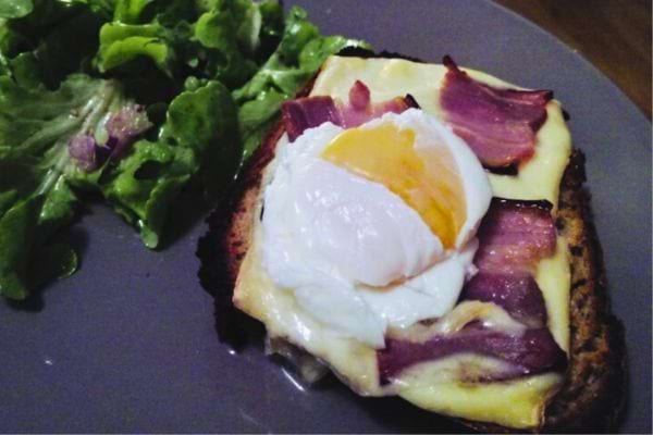 Tartine gratinée au fromage et bacon, surmontée d'un oeuf poché, avec salade.