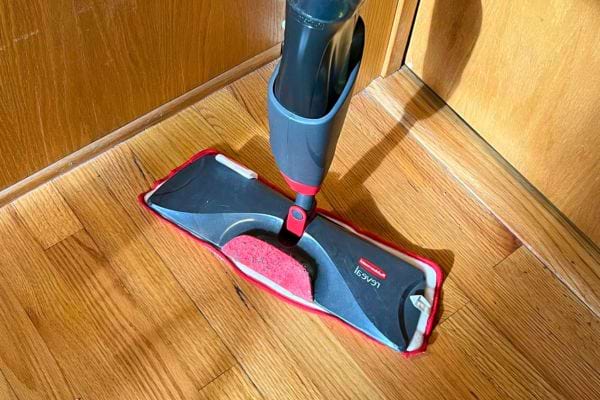 Une vadrouille spray avec un manche noir et rouge sur un parquet en bois.