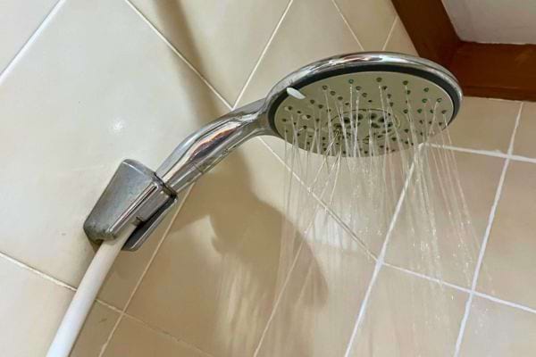Douche argentée fixée au mur avec des carreaux blancs.