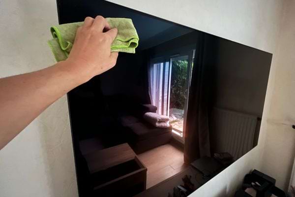 Main nettoyant un écran de télé avec un chiffon vert.