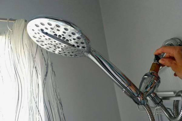 Pommeau de douche argenté tenu par une main.