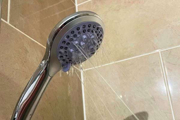 Pommeau de douche argenté sur un mur beige.