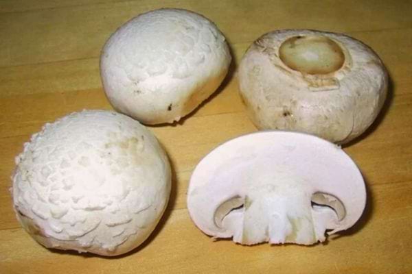 Quatre champignons de Paris, dont un coupé en deux, posés sur une surface en bois.