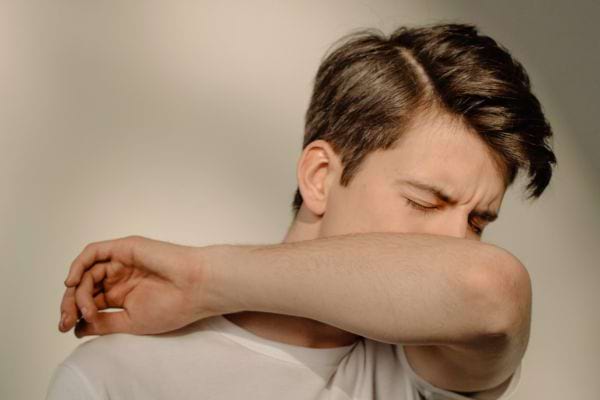 Un homme tousse dans son bras pour éviter la propagation de germes.