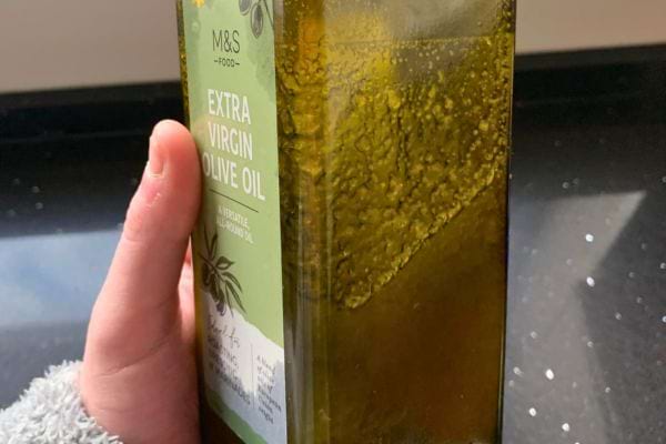 Bouteille d'huile d'olive extra vierge M&S tenue par une main.