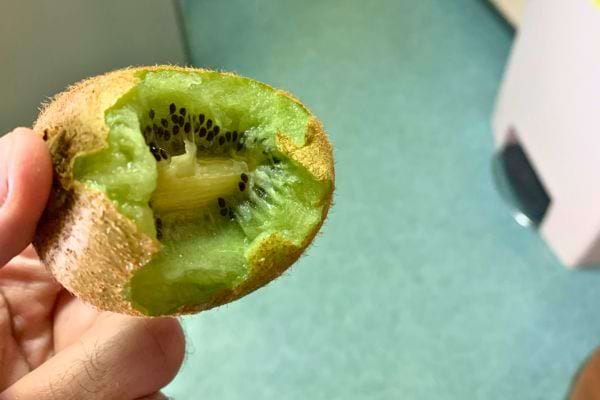 Kiwi vert partiellement mangé, tenu par une main.