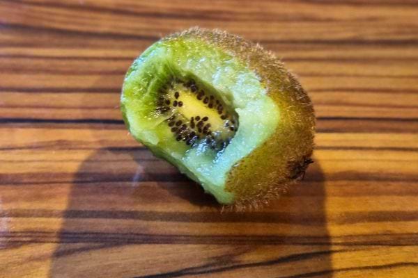 Kiwi vert mordu avec quelques graines visibles, posé sur une surface en bois.