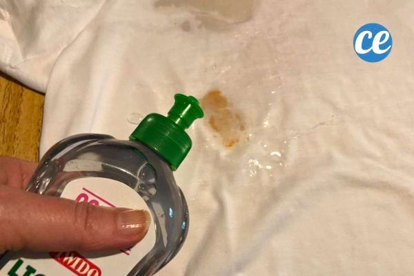 Liquide vaisselle appliqué sur une tache de ketchup sur un tissu blanc.