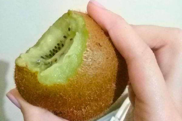 Kiwi vert avec une bouchée, tenu par une main, peau visible.