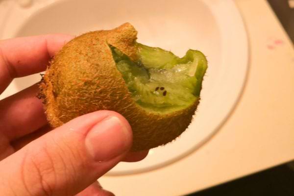 Kiwi vert avec une morsure, proche d'un lavabo, tenu à la main.