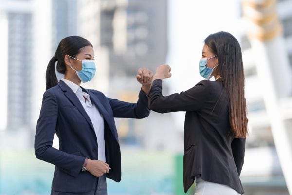 Deux personnes se saluent par le coude, portant des masques.