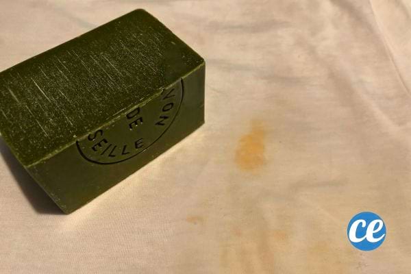 Savon de Marseille posé à côté d'une tache de ketchup sur un tissu blanc.