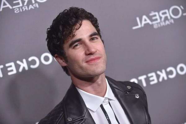 Darren Criss en veste en cuir noir, sourire discret.