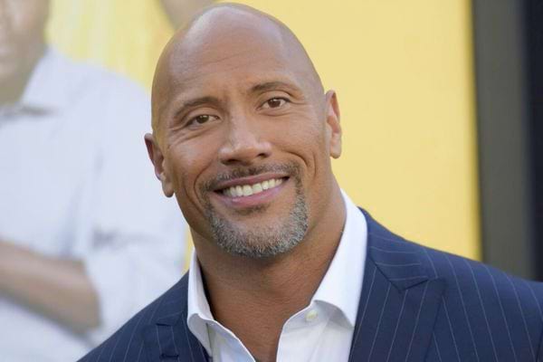 Dwayne Johnson souriant en costume à rayures.