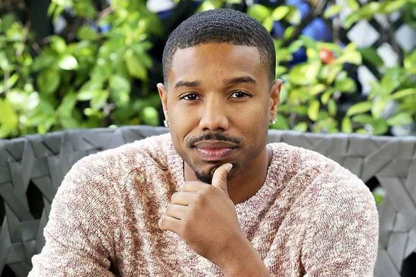 Michael B. Jordan posant en pull beige, souriant.