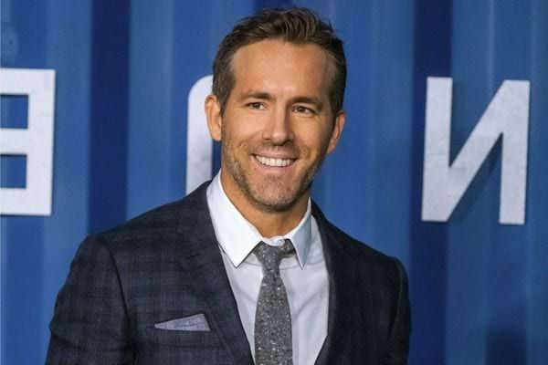 Ryan Reynolds en costume gris, souriant.