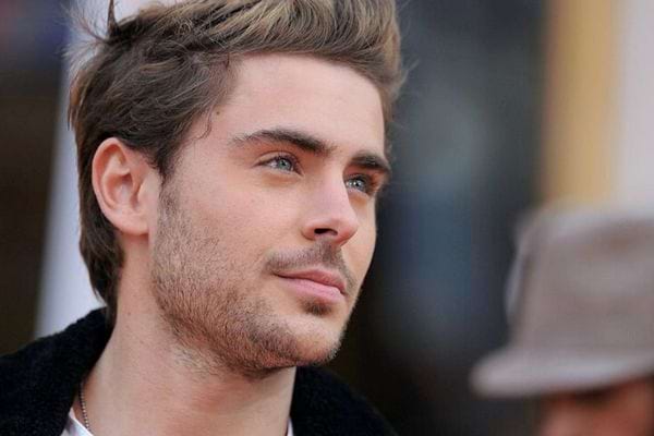 Zac Efron en veste noire, regard pensif.