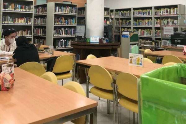 Bibliothèque calme avec tables et chaises jaunes, étagères de livres.