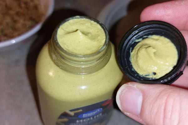 Bouteille de moutarde ouverte avec capuchon retiré, moutarde visible à l'intérieur.