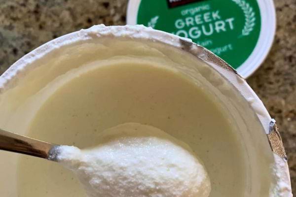 Cuillère plongée dans un pot de yaourt grec.