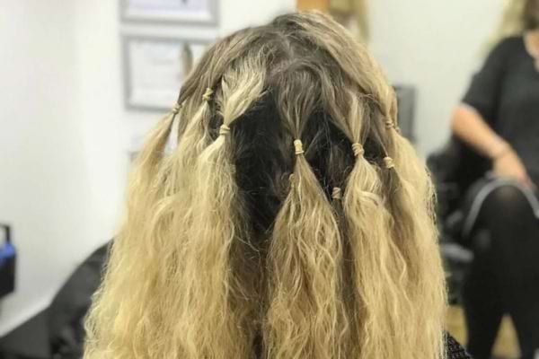 Femme vue de dos, cheveux blonds frisés attachés en petites sections.