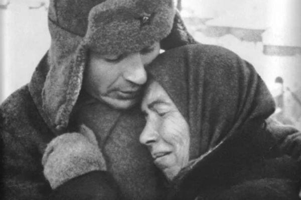 Homme en manteau militaire étreignant une femme âgée, en noir et blanc.