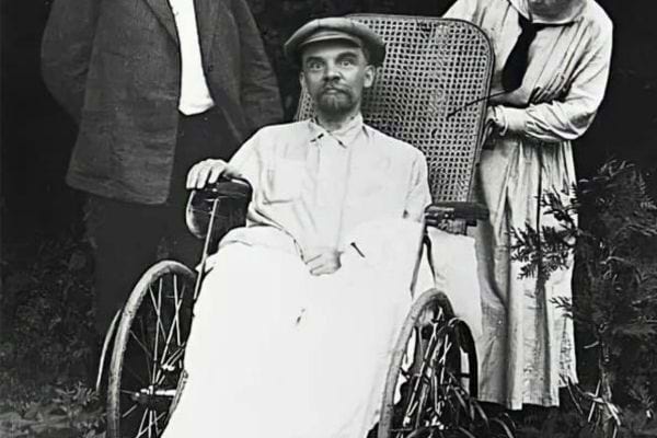 Homme barbu en fauteuil roulant, entouré de deux personnes debout.