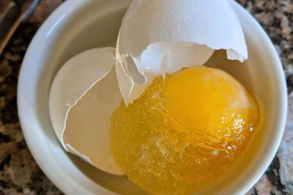 Un œuf congelé dans une coupelle, avec la coquille partiellement brisée.