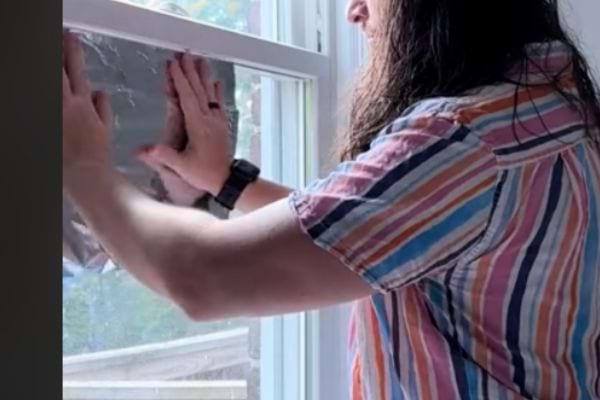 Personne appuie la feuille d'aluminium contre la fenêtre pour la fixer.