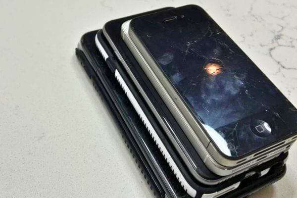 Pile de vieux iPhones avec écrans cassés.