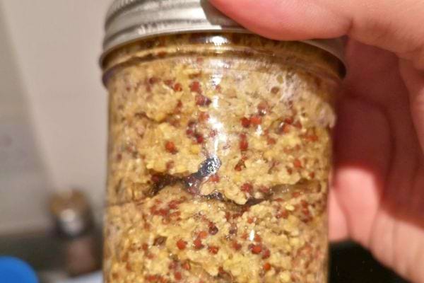 Pot de moutarde aux grains tenu dans une main.