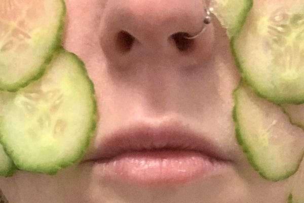 Rondelles de concombre posées sur un visage.
