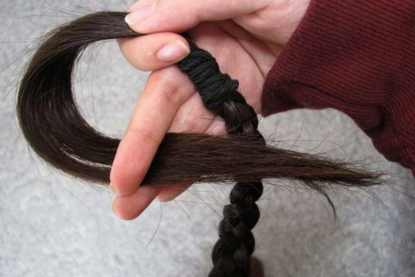 Main tenant une tresse de cheveux coupée, attachée par un élastique.