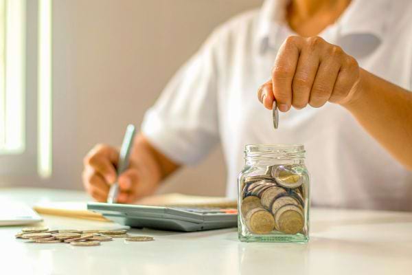 Un homme mettant une pièce dans un petit bocal en verre avec une calculatrice à proximité