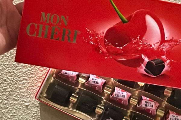 Boîte rouge Mon Chéri ouverte, montrant les chocolats alignés avec une cerise en illustration.