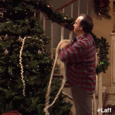 Un homme qui balance une guirlande de manière négligée sur un sapin gif