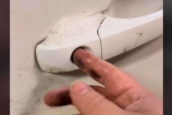 Doigt essuyant la saleté accumulée sur une poignée de porte blanche de voiture.