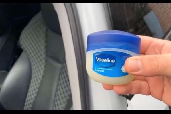 Main tenant un petit pot de Vaseline bleu devant une voiture.