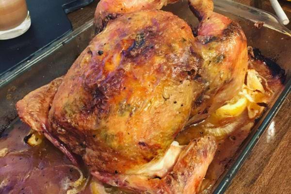 Poulet rôti entier dans un plat en verre avec jus de cuisson.