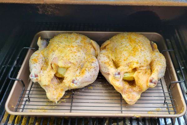 Deux poulets entiers assaisonnés prêts à cuire sur une grille.