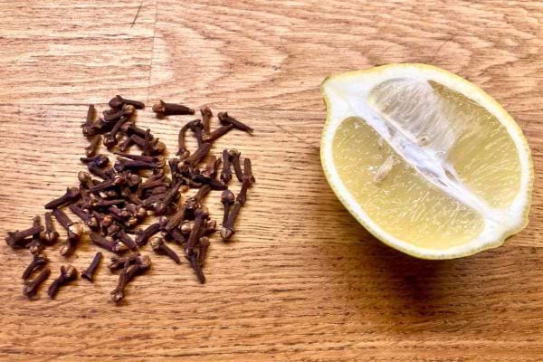 Une moitié de citron à côté de clous de girofle éparpillés sur bois.