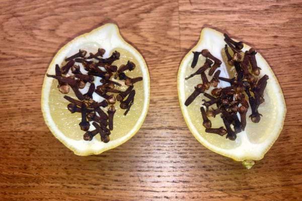 Clous de girofle posés sur une moitié de citron, vue de dessus sur une table en bois.
