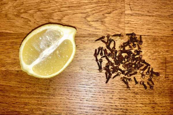 Une moitié de citron et des clous de girofle éparpillés sur une table en bois.